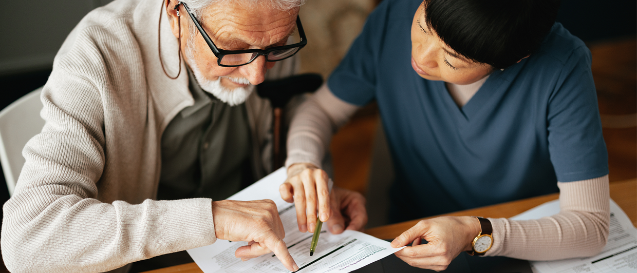 An elderly man and a healthcare worker review medicare advantage plan together at a table, both pointing to information on a document.