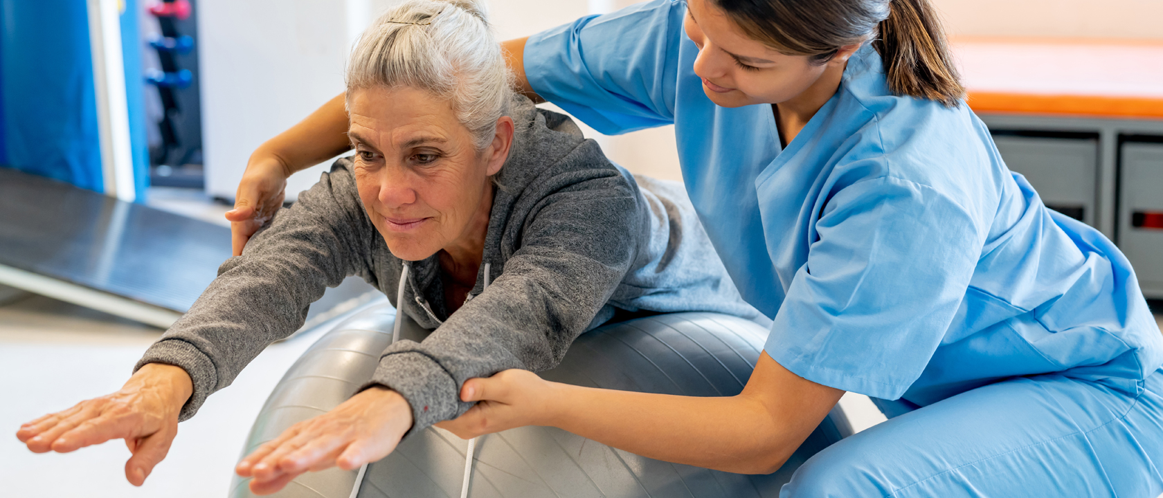 Physical therapist helping woman on exercise ball